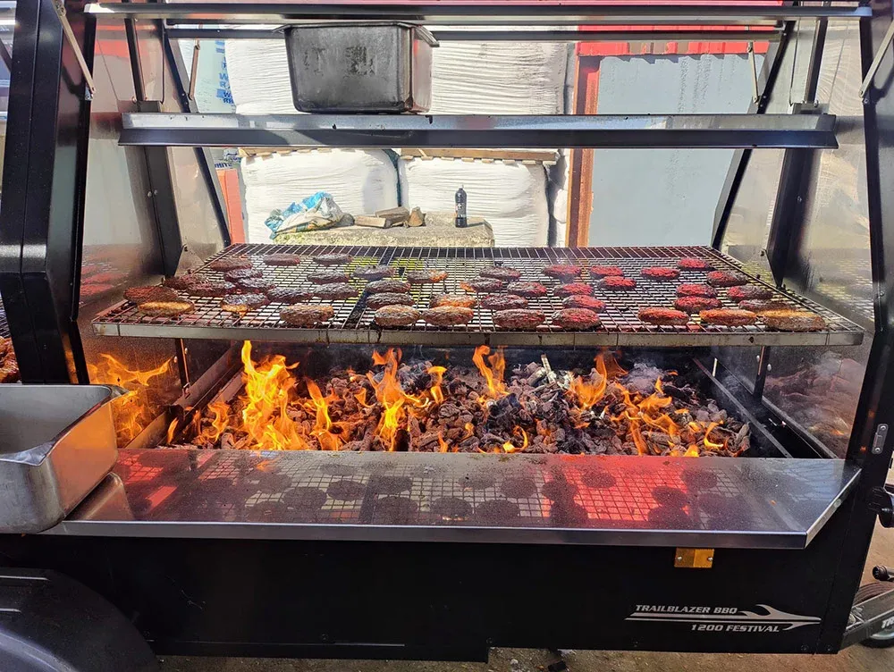 Charcoal grill loaded with sizzling meat at a Castlemeats BBQ