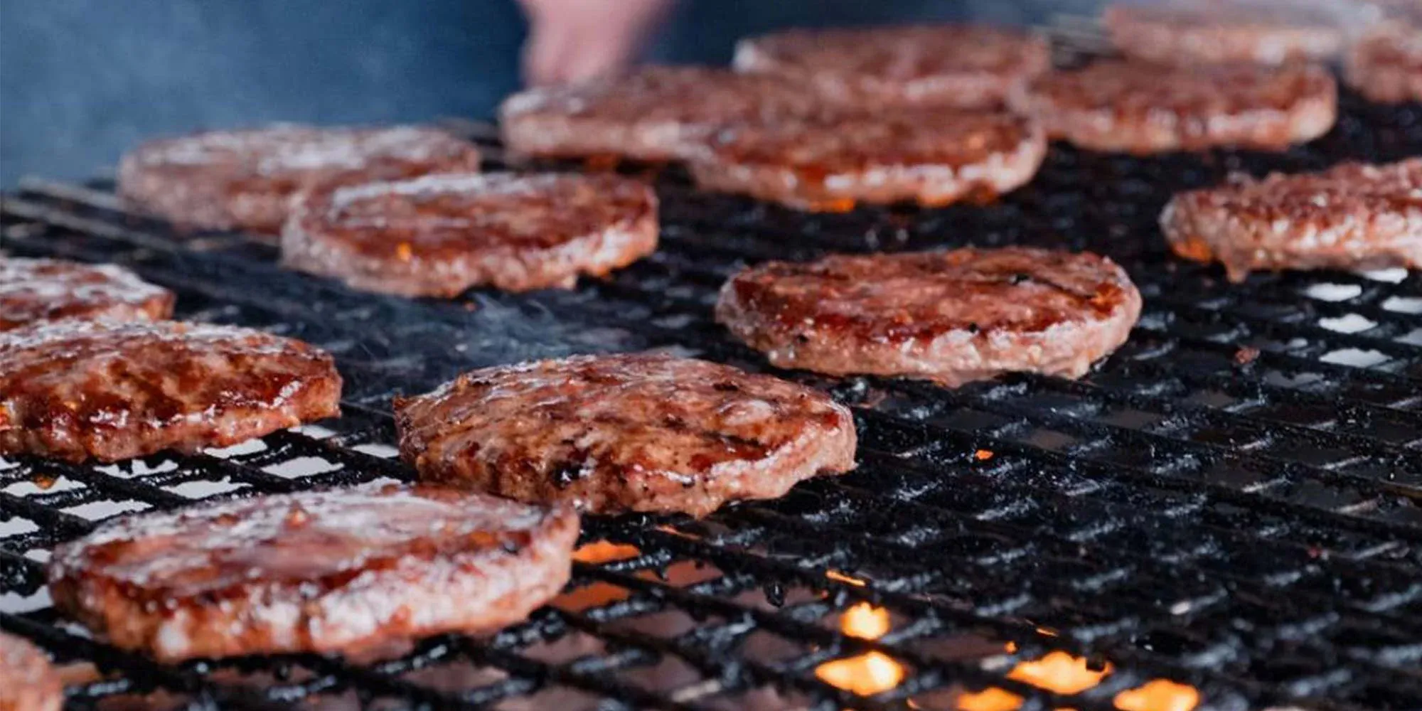 Rows of burgers cooking on a charcoal grill